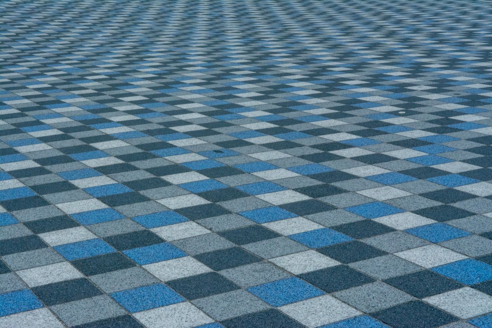 Square pavers in gray, charcoal and blue laid in a grid, showing how a mixed-color square paver pattern looks across a plaza