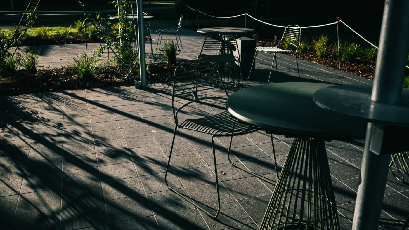 Patio of gray square concrete pavers laid in a straight grid with metal cafe tables and chairs in late afternoon shade