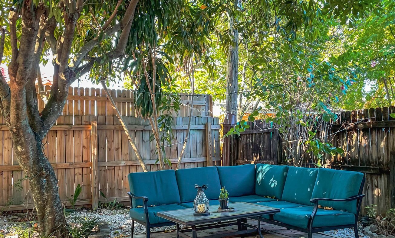 Small backyard patio of square concrete pavers in blended colors under a tree, with outdoor sofa and gravel surround