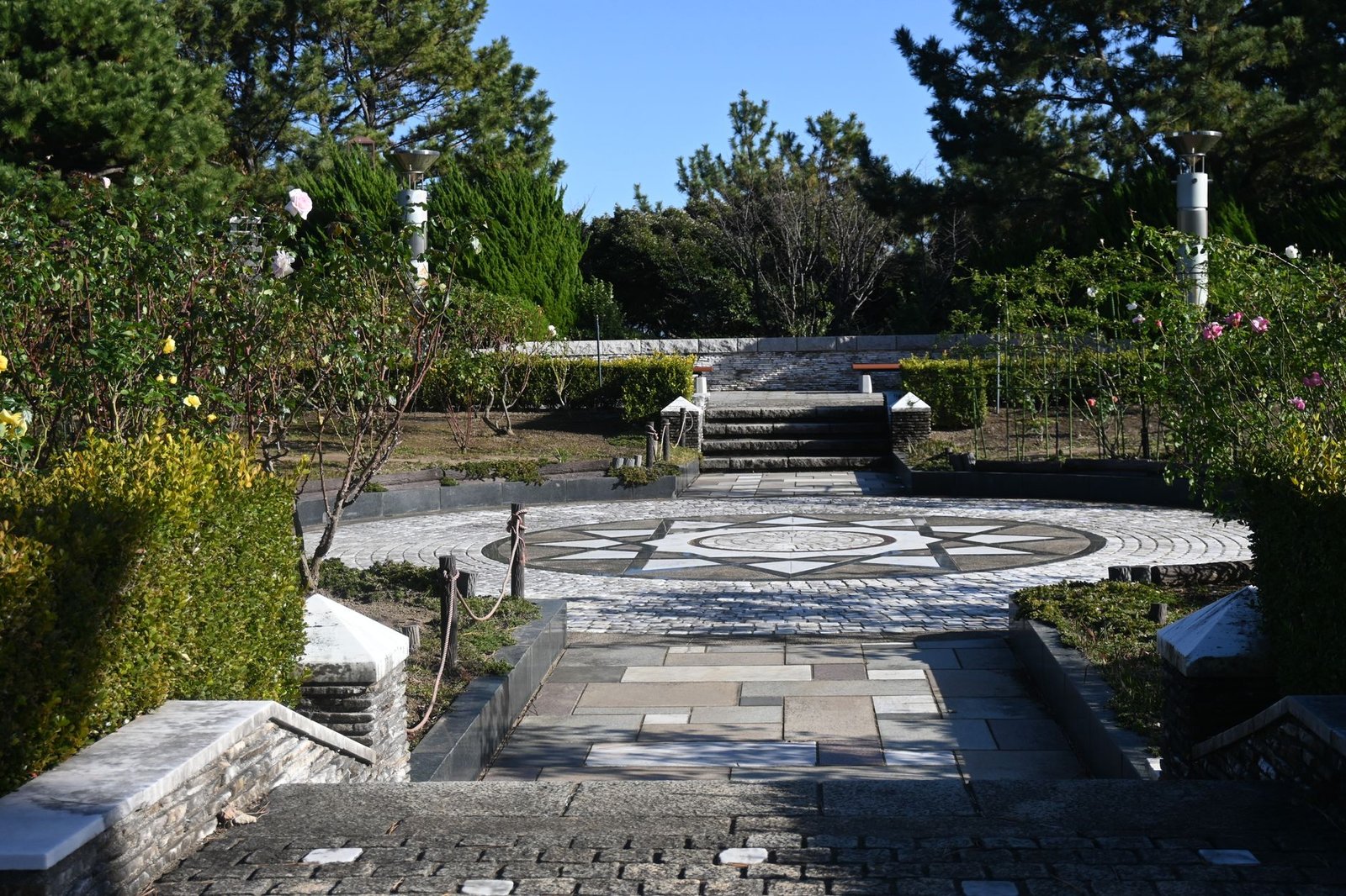 Garden with a stone path leading to a circular mosaic paving medallion set within a larger paved area