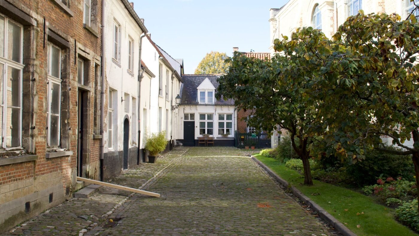 Old cobblestone lane between brick houses with a lawn and trees, showing traditional granite cobble paving