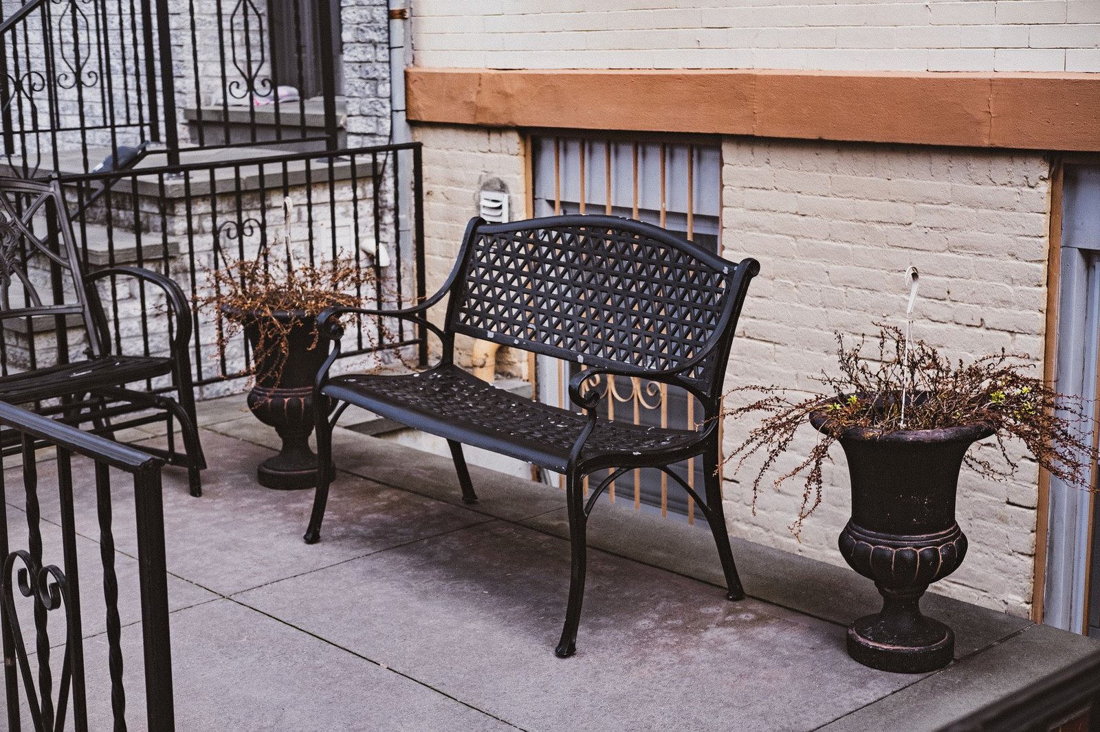 Concrete patio slab with a metal bench and potted plants against a painted brick wall