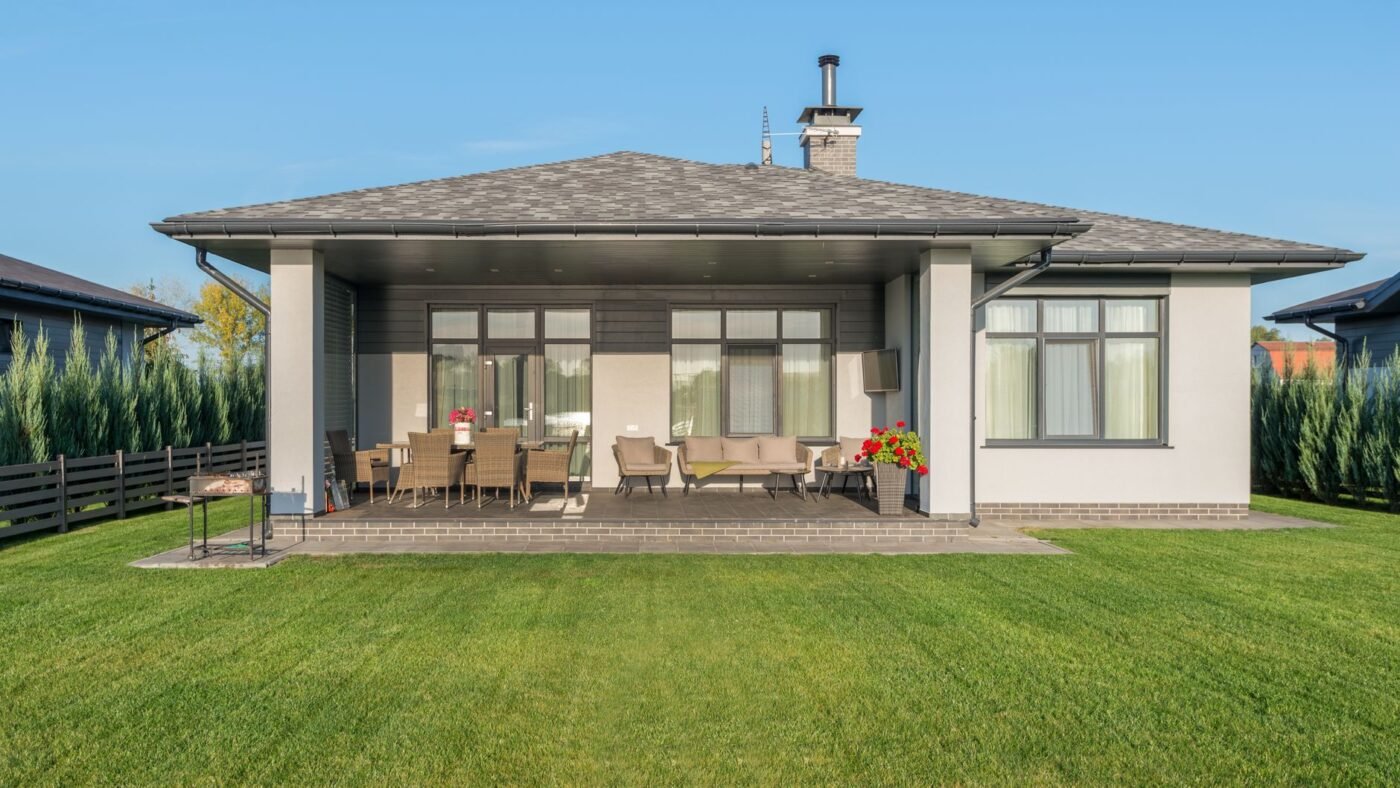 Covered backyard patio of a single-story house with a contrasting border course along the lawn edge