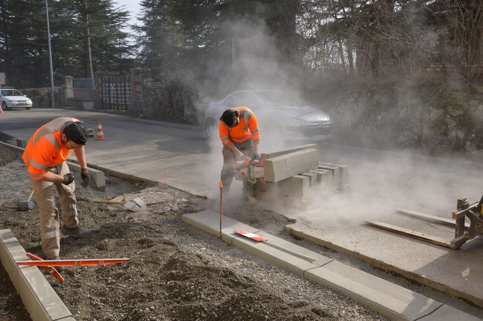 Two workers trimming concrete curb blocks with a cut off saw, cutting dry and raising a thick cloud of silica dust