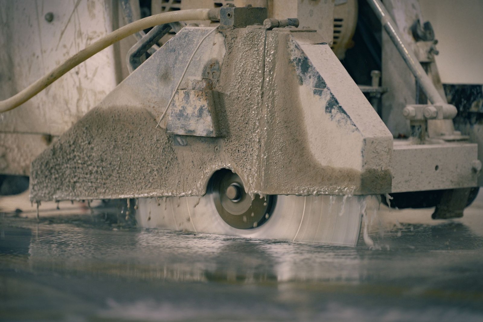 Walk-behind concrete saw cutting wet, with water and slurry flowing around a large diamond blade