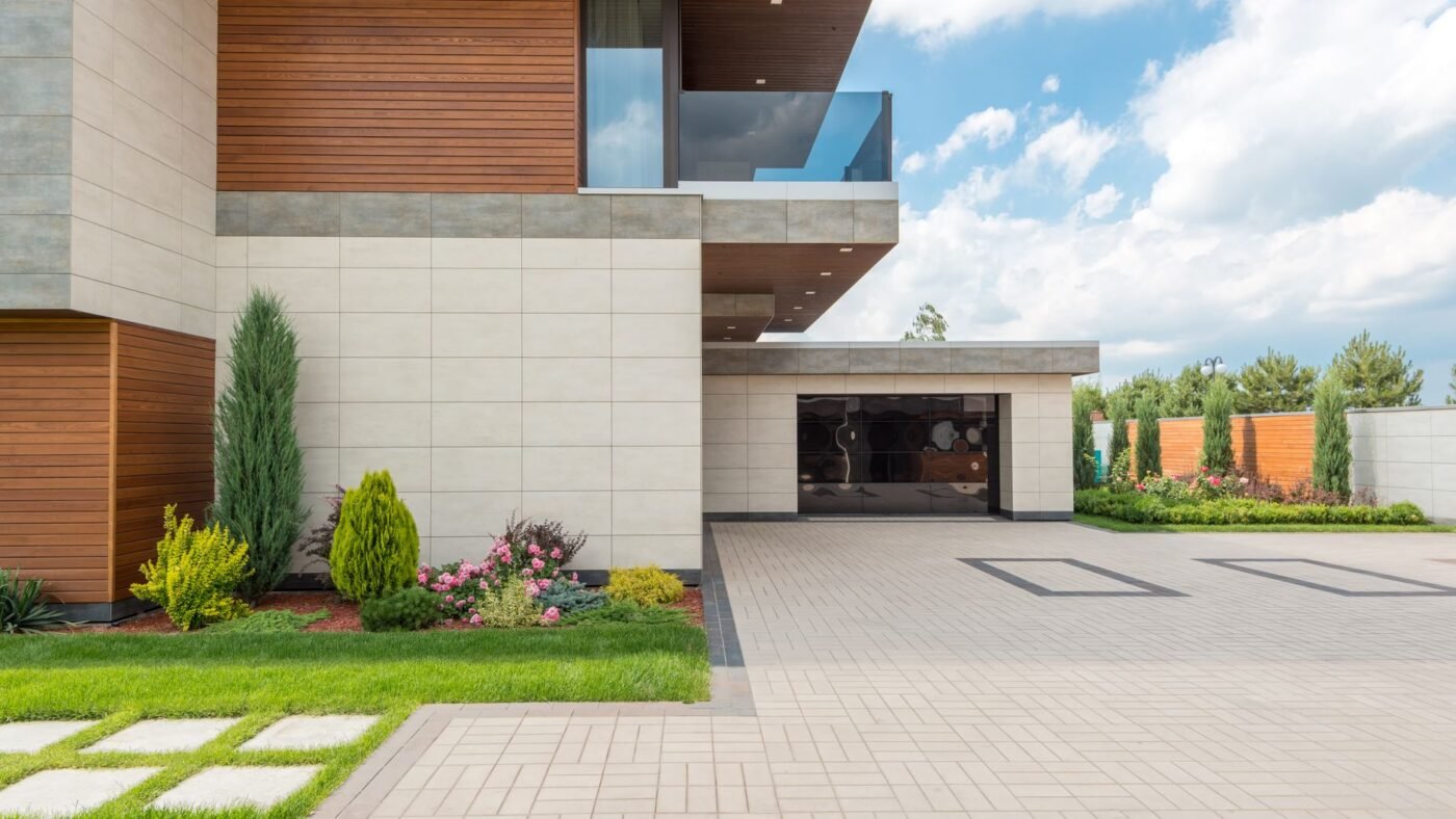 Light gray paver driveway in front of a modern house, framed by a darker border course along the lawn edge