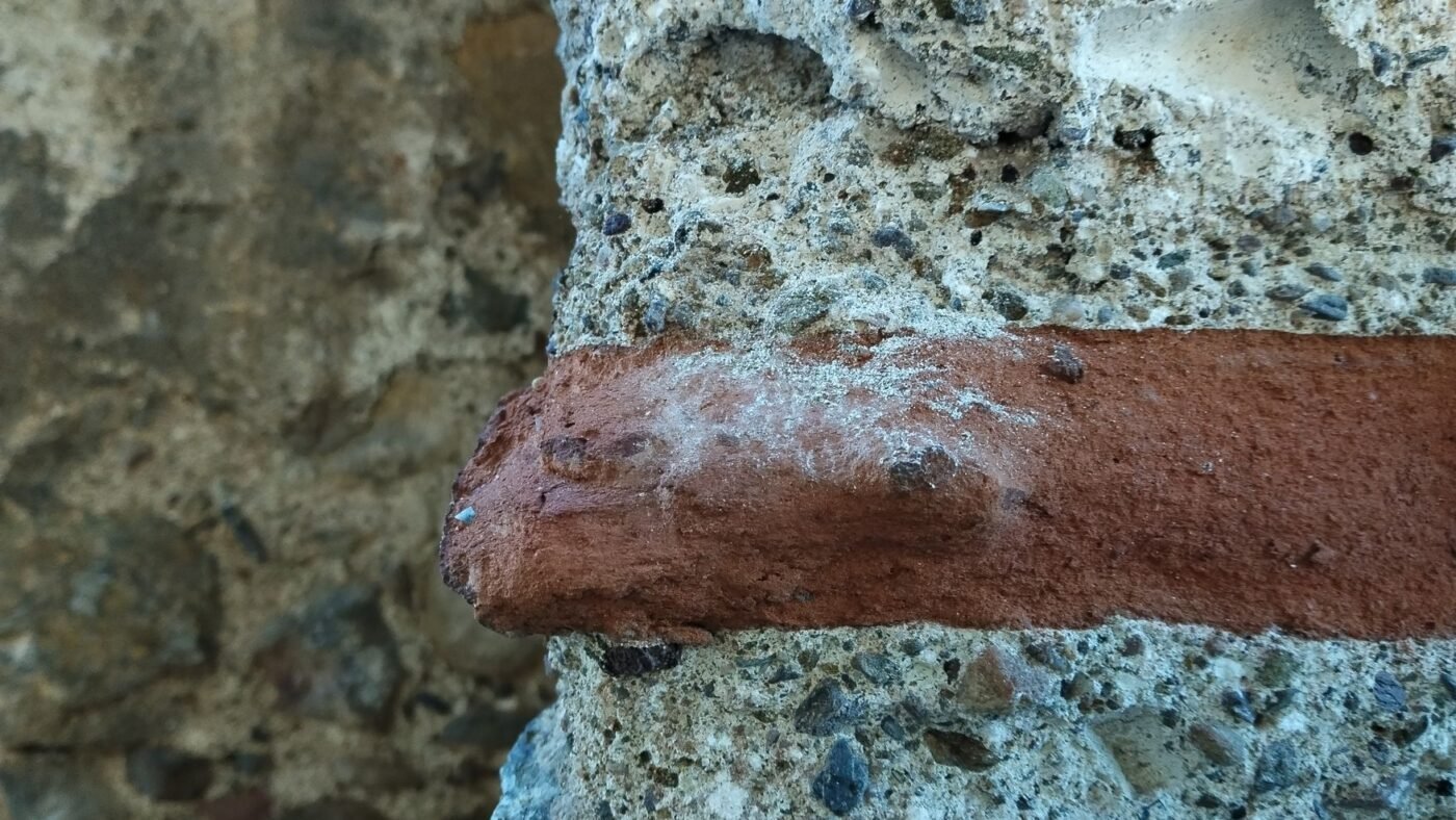 White efflorescence salt deposit blooming on the face of a clay brick set in concrete