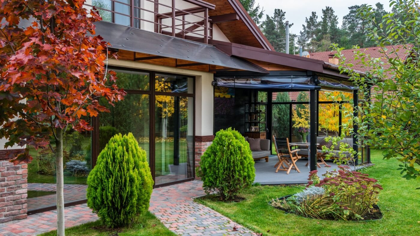 Modern house with a glass-walled garden room, a tumbled paver walkway through the lawn and shaped shrubs, showing hardscape and softscape together