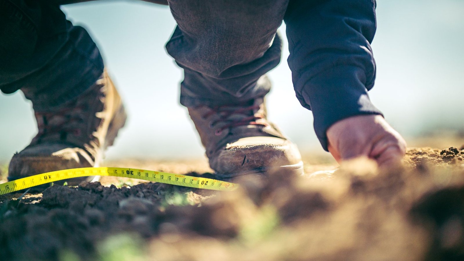 Person in work boots measuring bare ground with a yellow tape measure before ordering pavers