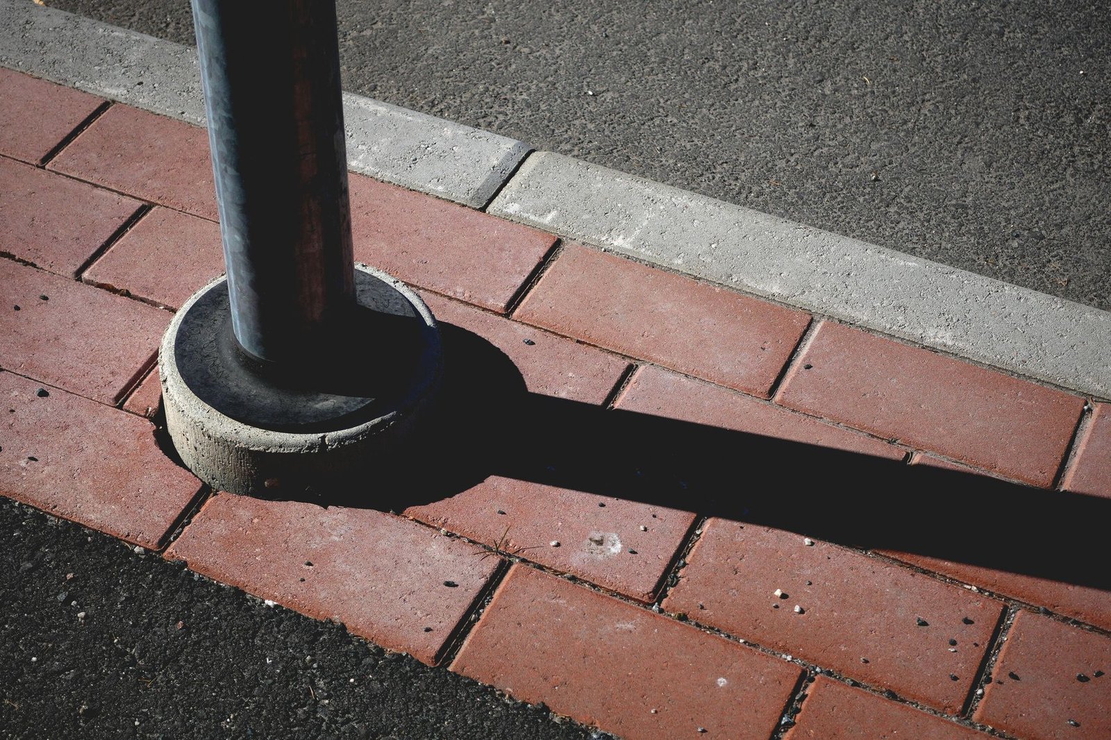 Red running bond pavers cut around the round base of a metal post next to a curb