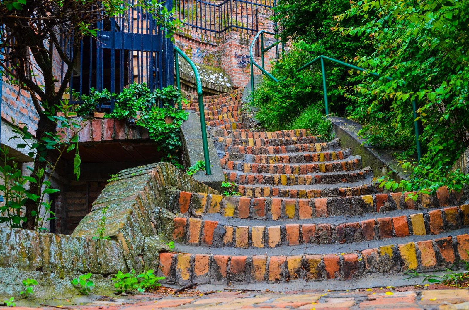 Brick steps climbing a slope with a stone side wall and metal handrails, a flight of paver steps built into a hillside