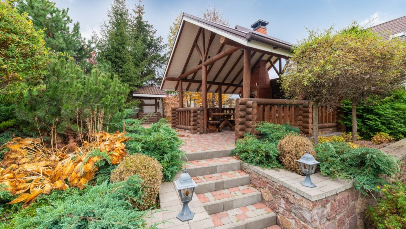 Paver steps with block side walls climbing from a garden path to a raised paver patio and wooden pavilion