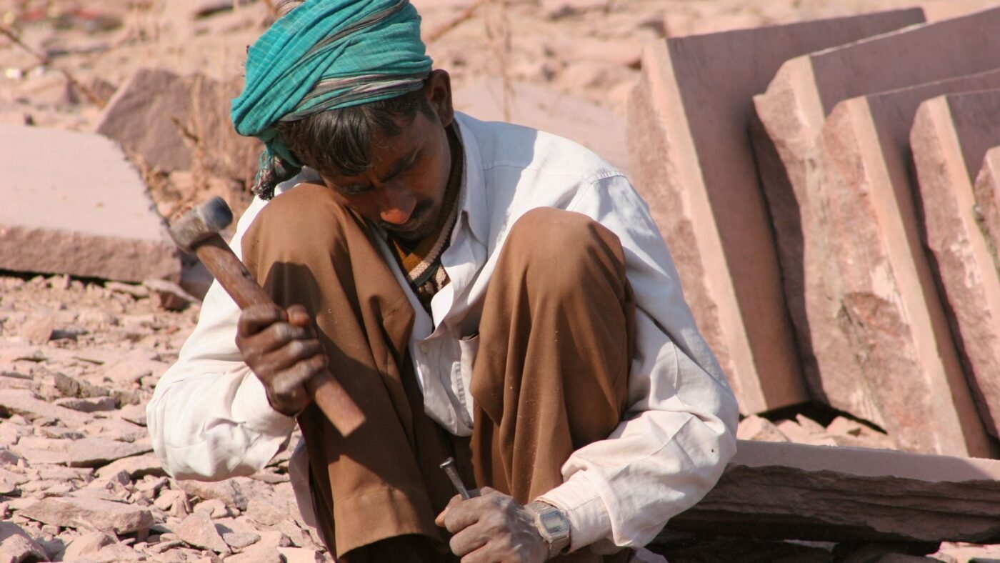 Stonemason crouching over a stone slab and splitting it by hand with a hammer and chisel, no saw involved