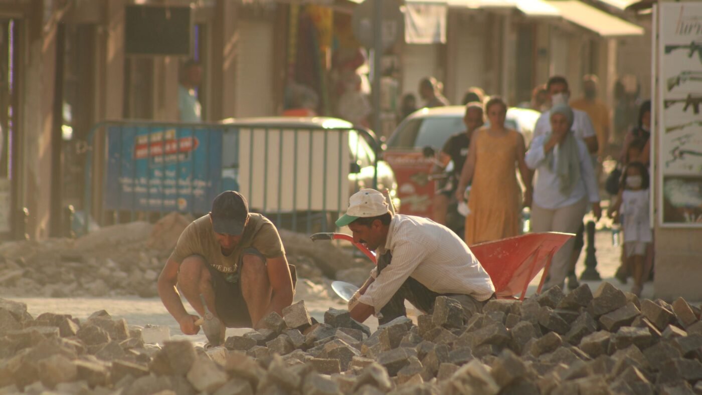 Workers lifting and stacking paving stones to rebuild the bed under a sunken section of pavement