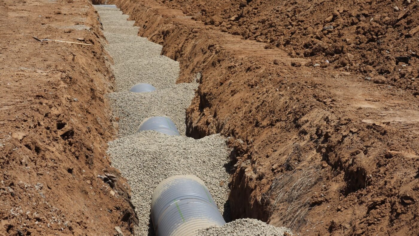 Narrow trench with drainage pipe bedded in gravel, the kind of confined space where a jumping jack rammer outperforms a plate compactor