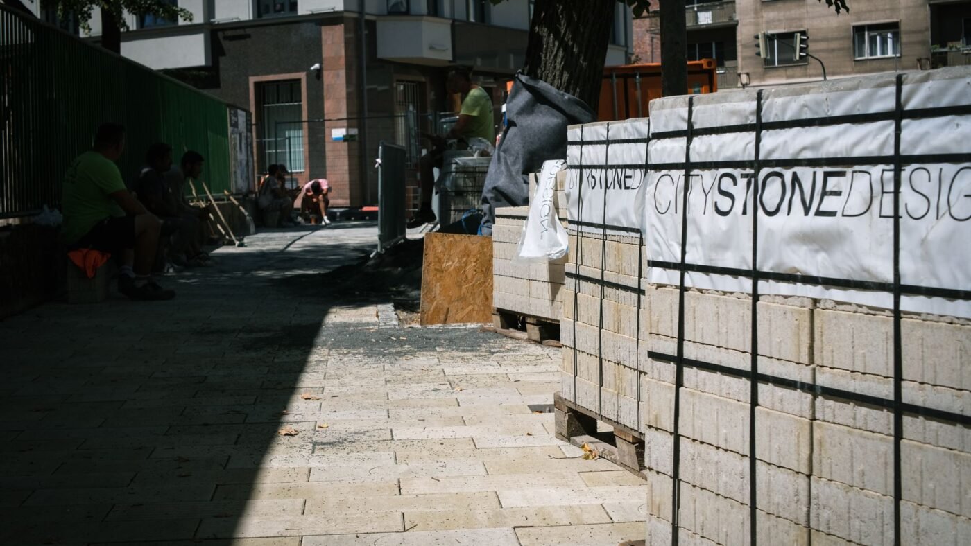Paving project in progress with pallets of new pavers stacked beside a freshly laid section, the stage where fabric and base go down