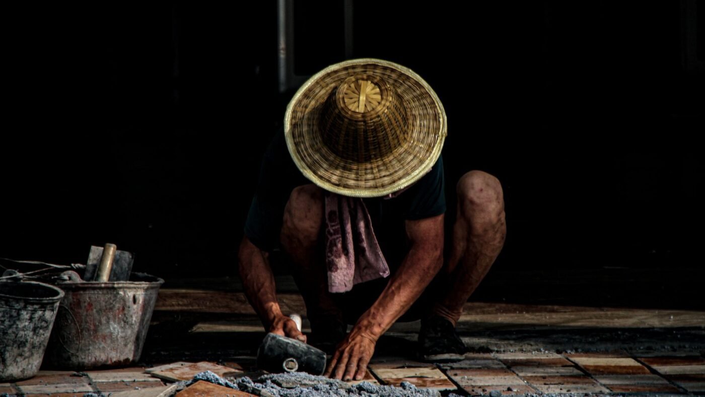 Mason tapping pavers into a mortar bed with buckets of mortar nearby, the first stage of a mortar-set paving job with mortar joints