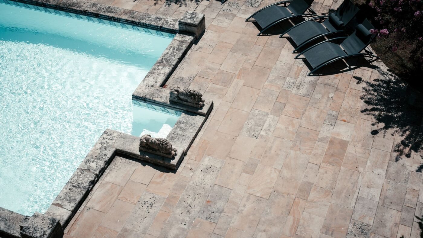 Tumbled cream natural stone pavers in a random pattern around a swimming pool with stone coping and lounge chairs