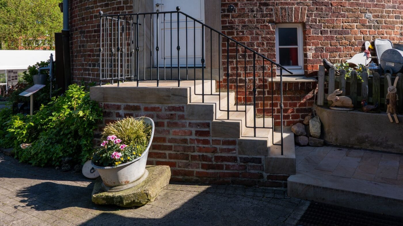 Plain concrete entry steps with a metal railing beside a brick house, the kind of steps a paver overlay can cover