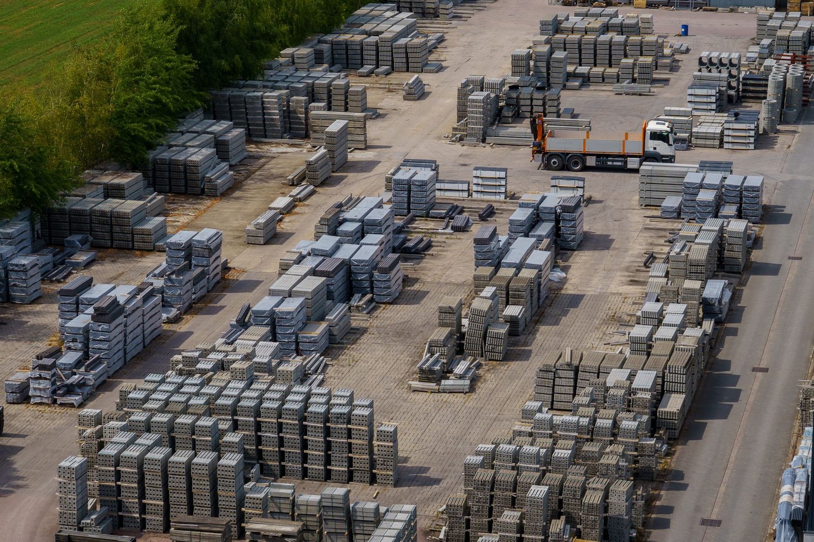 Aerial view of a paver manufacturing yard with rows of stacked pallets of pavers and blocks and a delivery truck