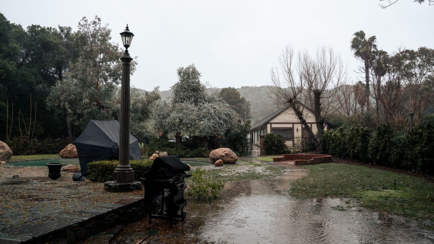 Backyard stone patio and lawn under standing water after a storm, showing why patio drainage has to be planned