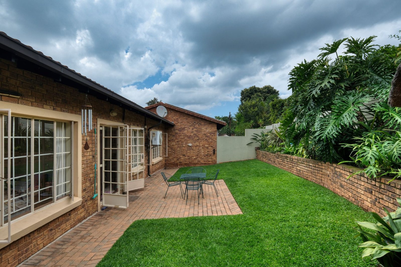 Brick patio with table and chairs meeting a green lawn, framed by a low brick garden wall