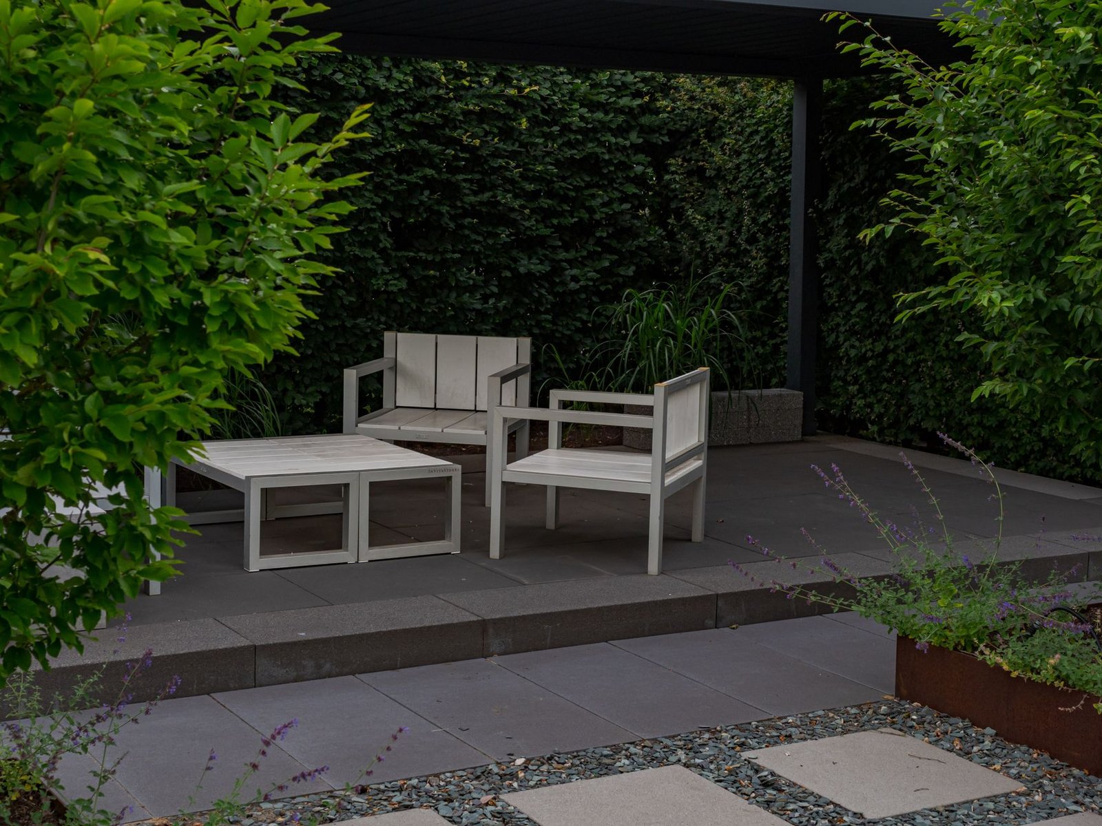 Modern patio laid with large-format gray slabs under a covered pergola with white outdoor furniture