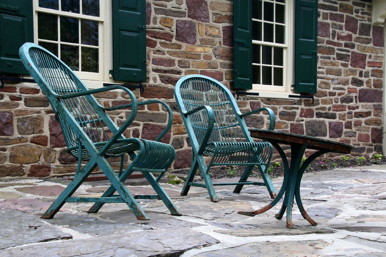 Flagstone patio in front of a stone house with two green metal chairs and a small table
