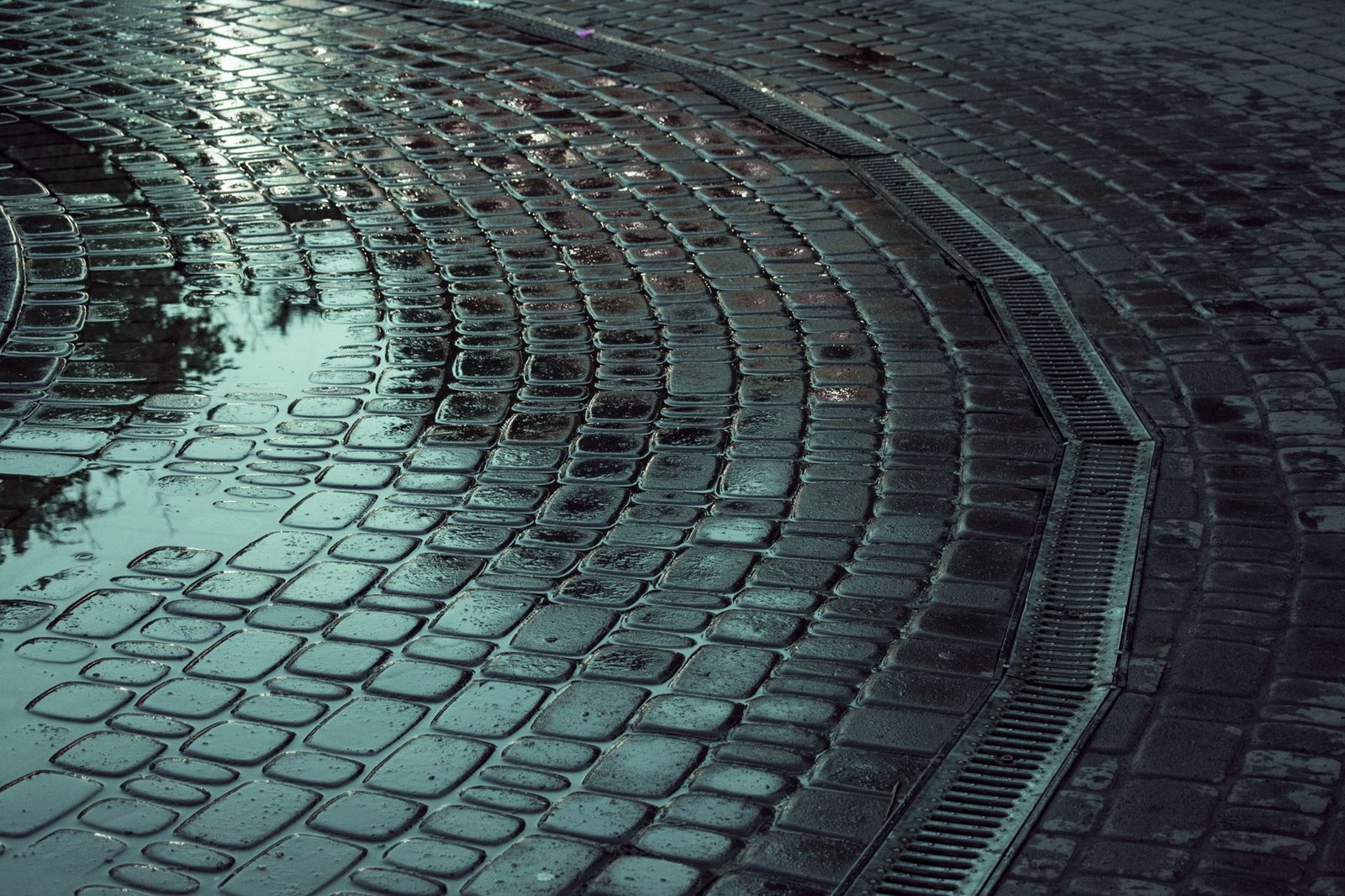 Wet paver surface after rain draining toward a channel drain, showing why a paver base must shed water