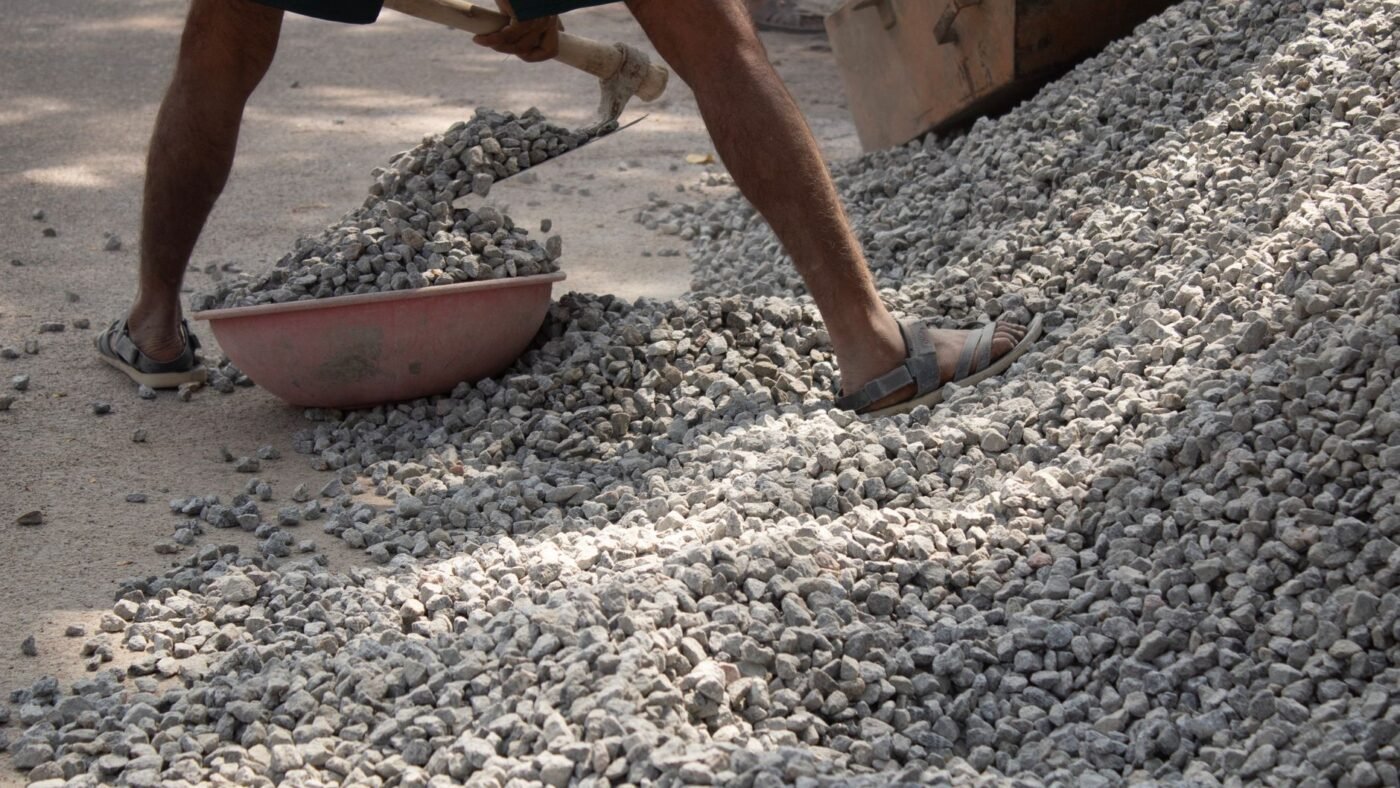 Worker shoveling angular crushed stone from a pile, a common paver base material for patios