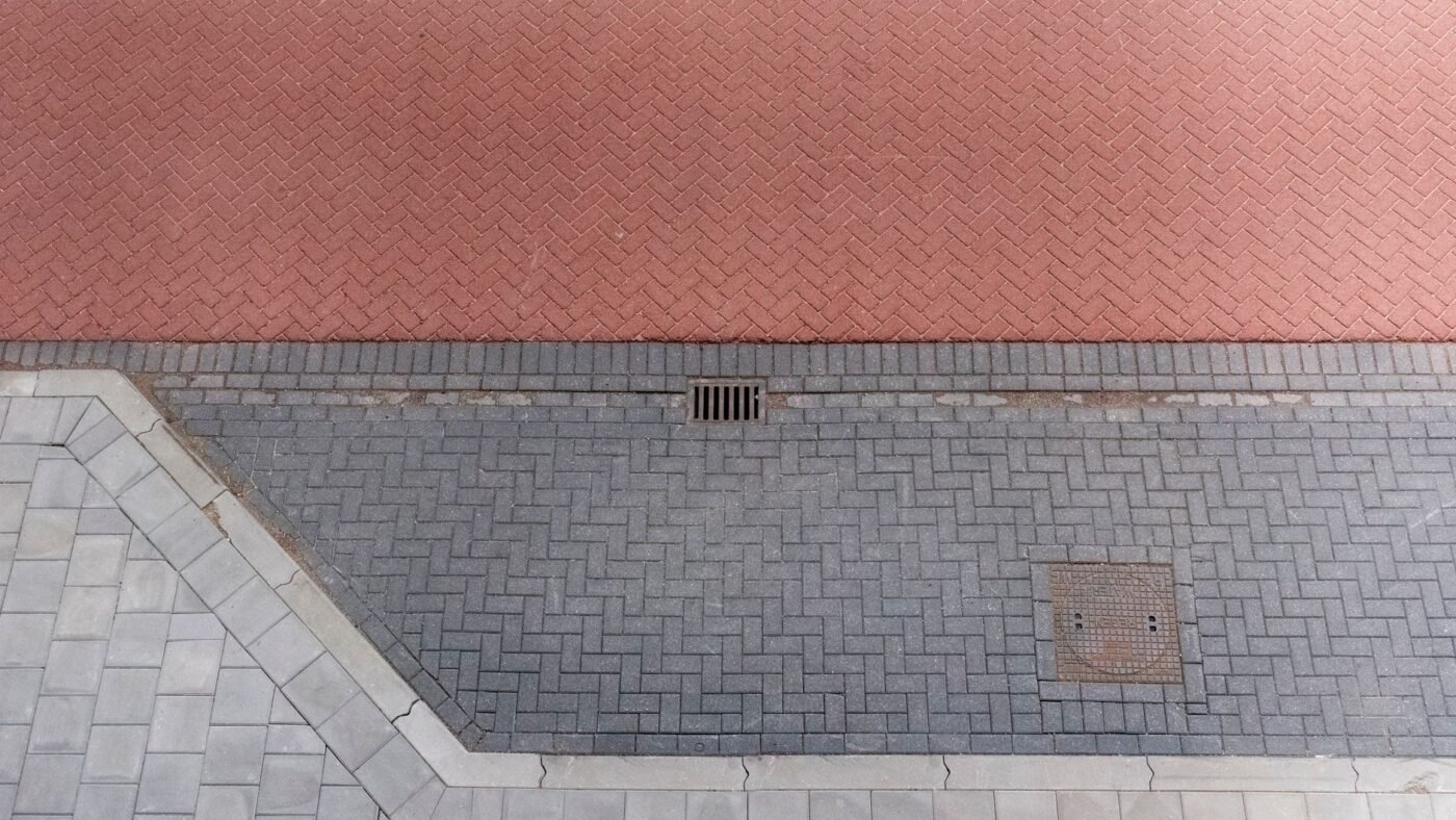 Overhead view of herringbone paving in red and gray with darker paver border rows framing each area