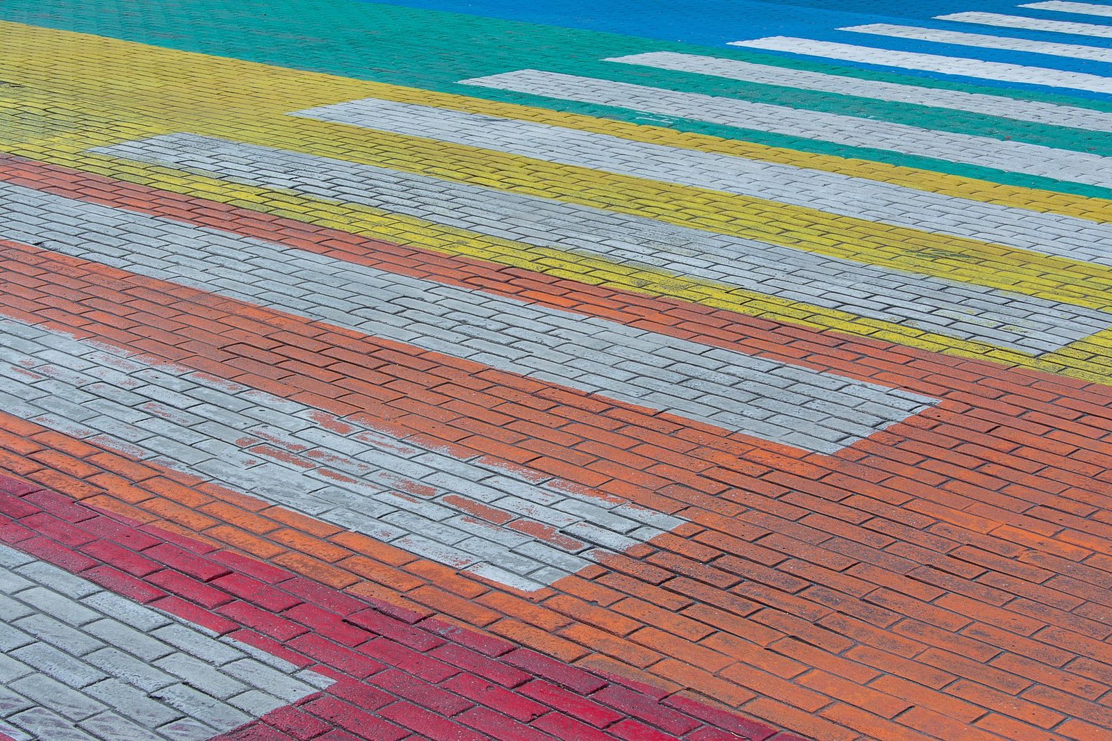 Rectangular concrete brick pavers in red, orange, gray and yellow laid in running bond across a paved crossing