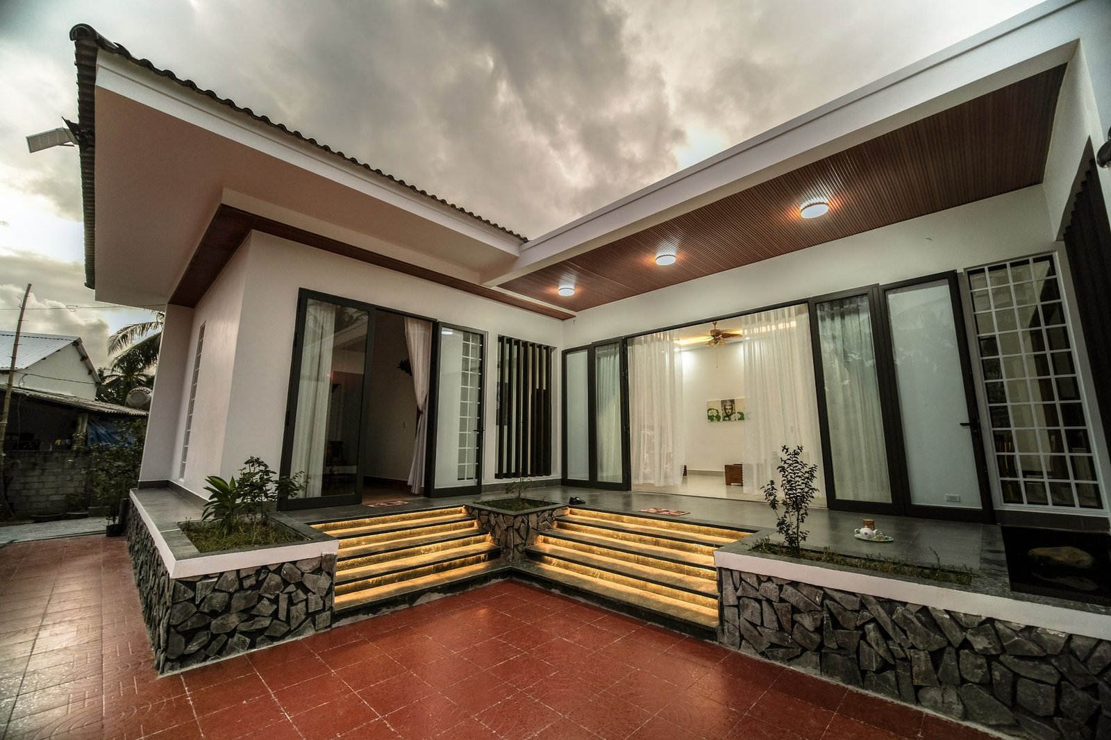 Courtyard paved with red square pavers in front of a modern house with lit steps
