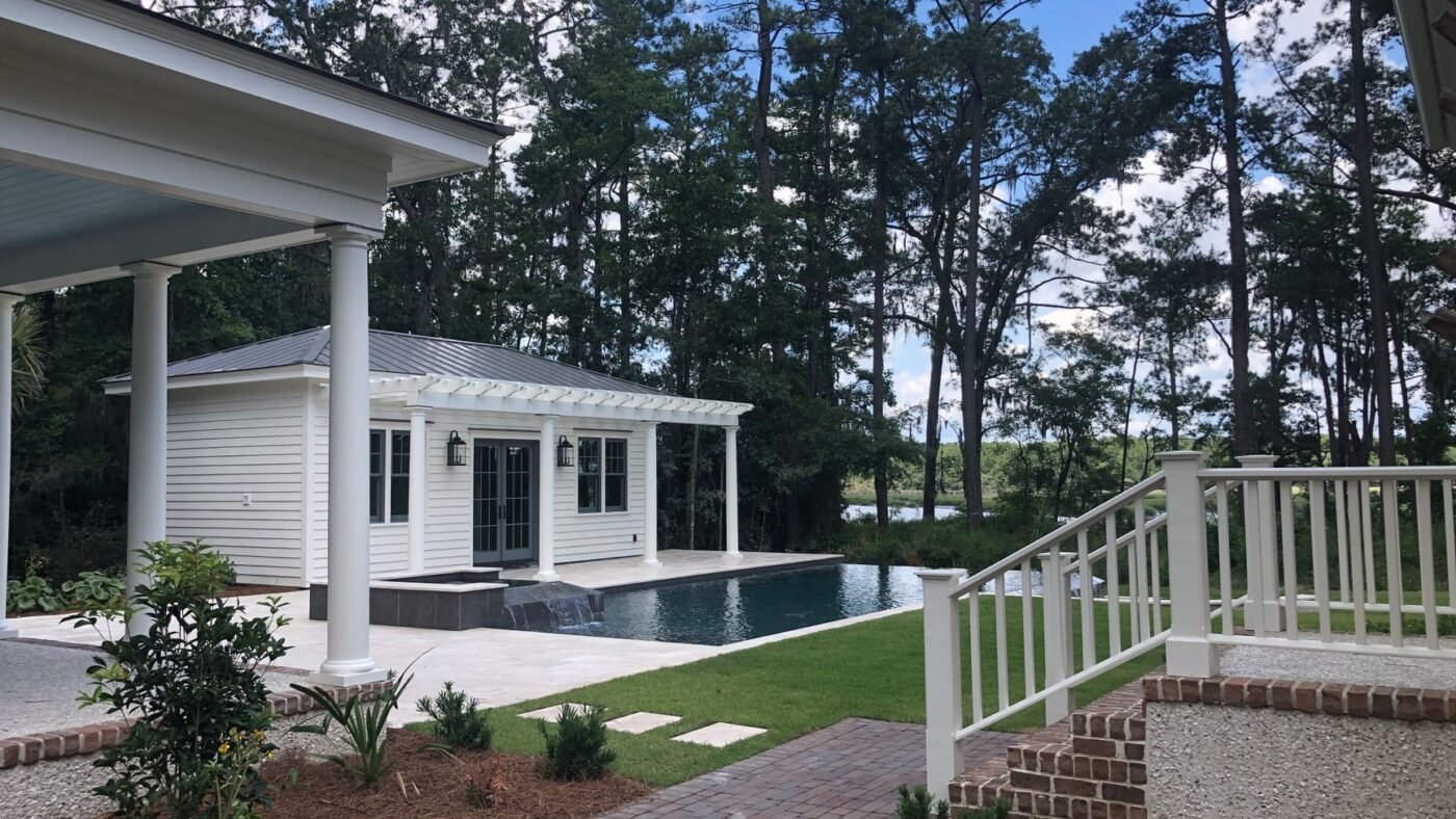Red brick paver walkway leading to a white house with a light-colored pool deck, showing paver colors chosen to suit the house