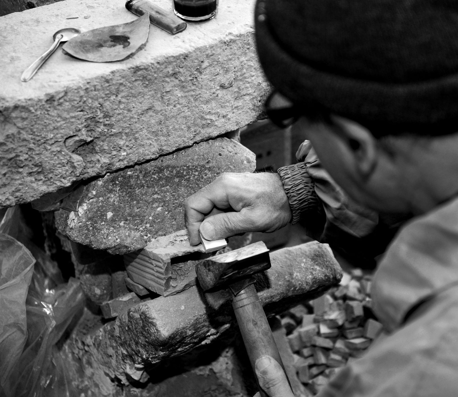 Stonemason holding a chisel against a stone block and striking it with a hammer to split it