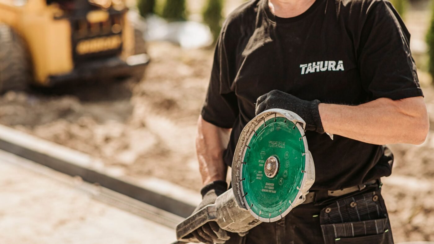 Landscaper on a site holding a large angle grinder fitted with a segmented diamond blade, one of the common paver cutting tools