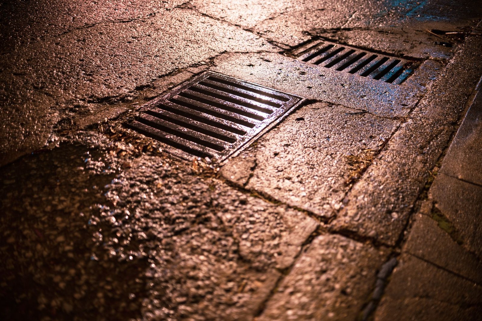 Rectangular metal drain grates set into stone paving, the way a patio catch basin sits flush in a paver surface