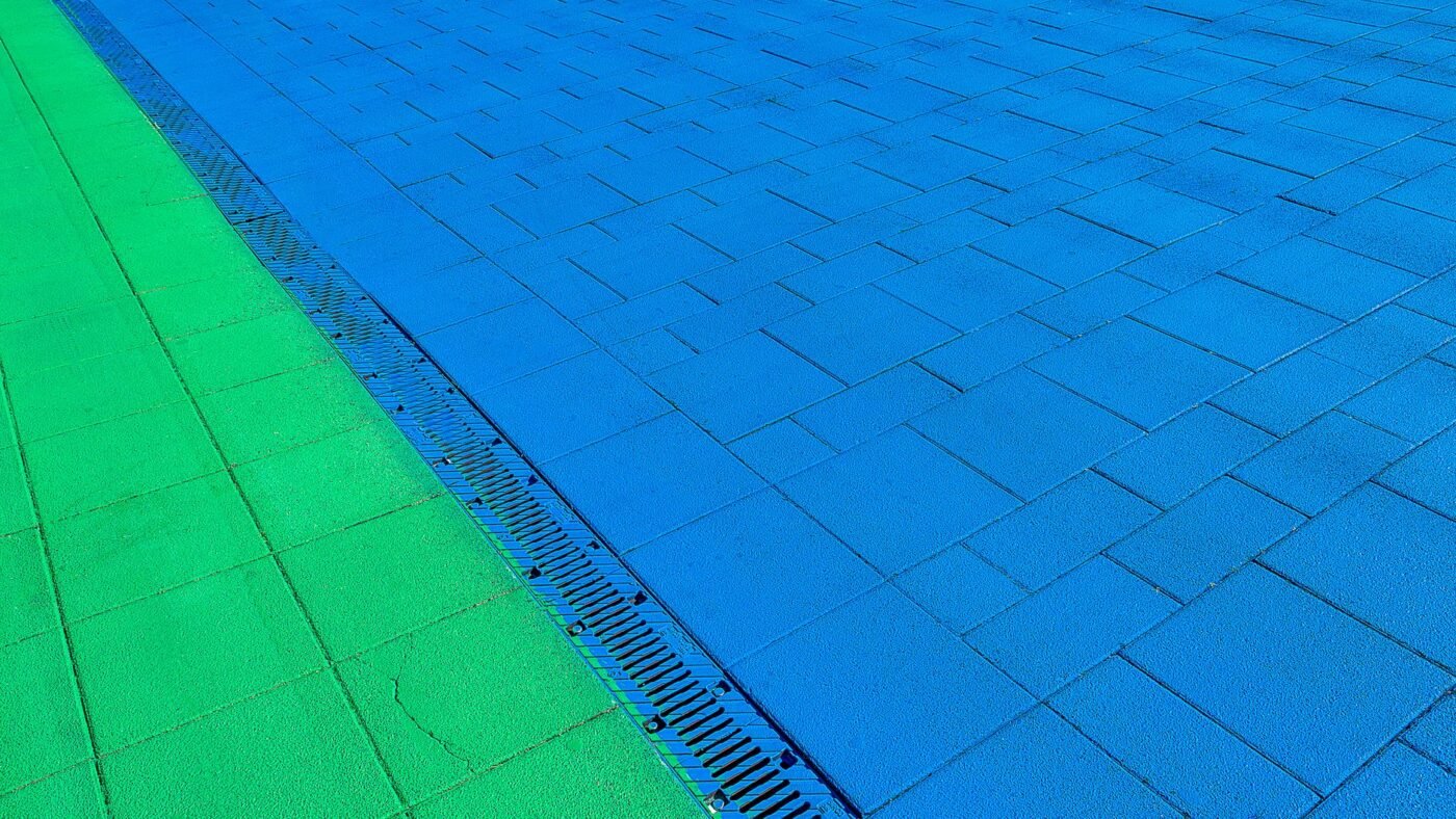 Linear channel drain with a slotted metal grate running between two areas of concrete pavers