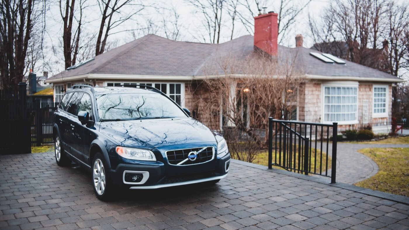 Dark blue car parked on a gray cobble-style paver driveway in front of a brick cottage