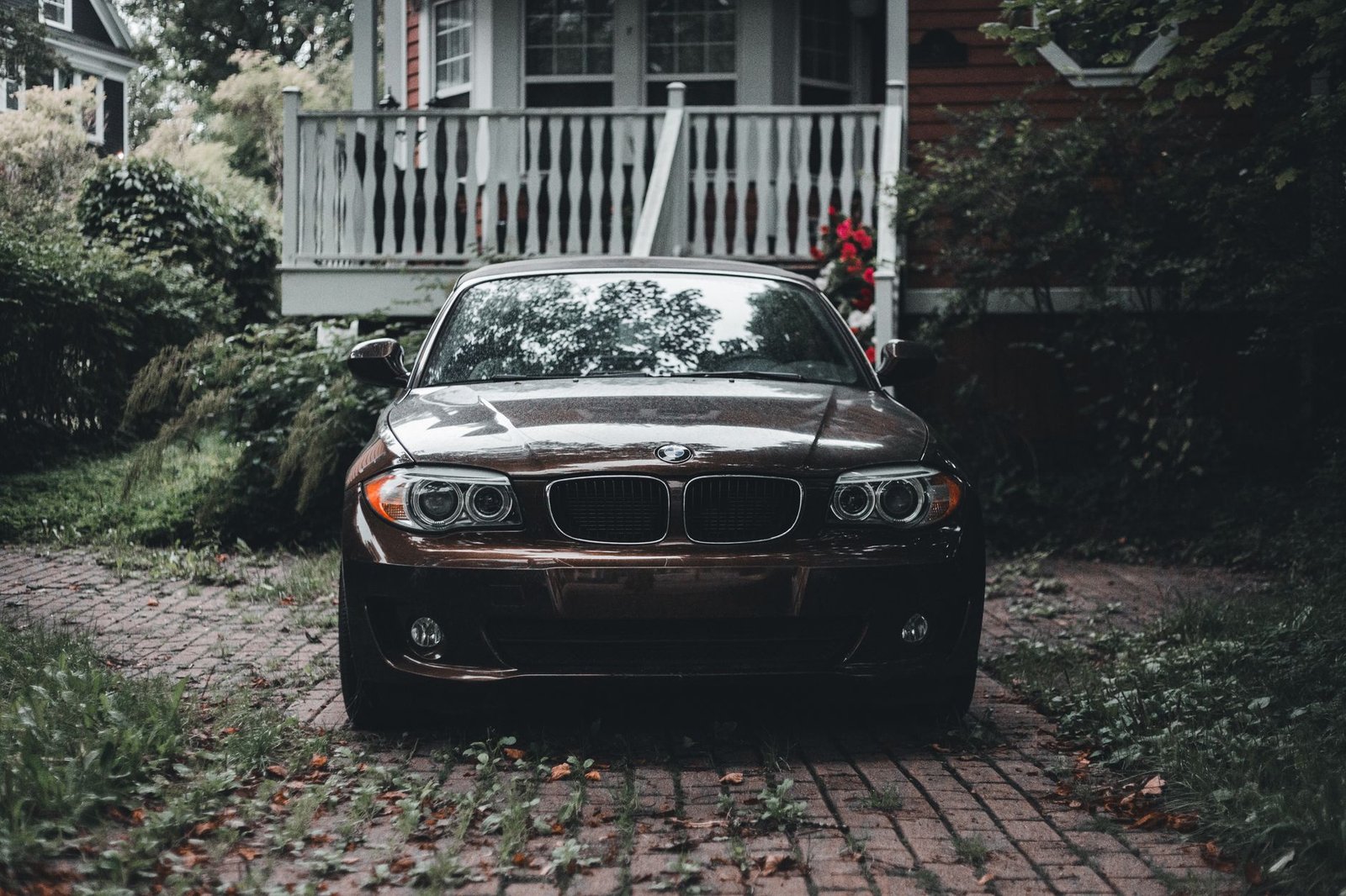 Dark sedan parked on an older brick paver driveway in front of a house