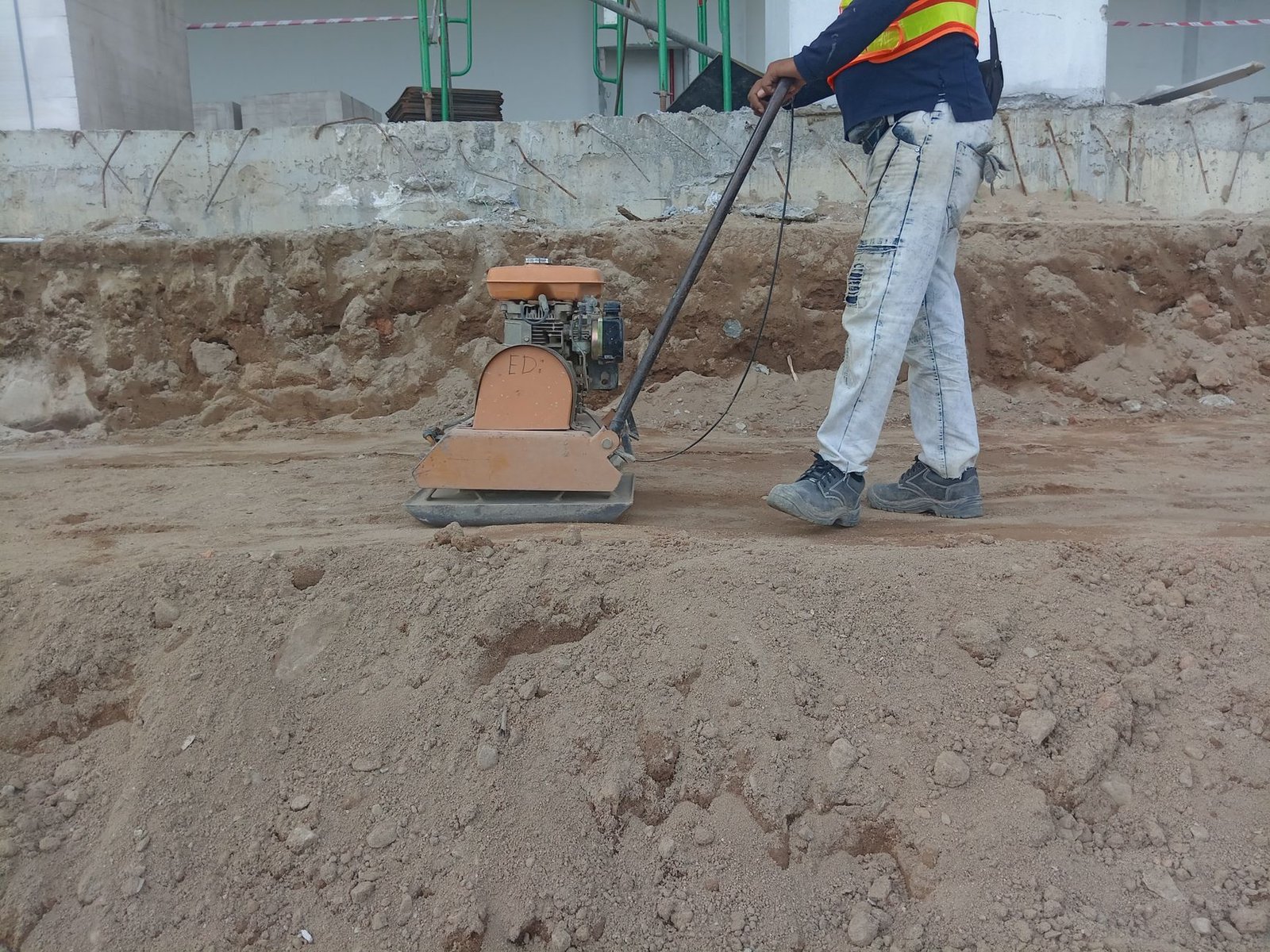 Worker running a plate compactor over bare soil to firm the subgrade before paver installation