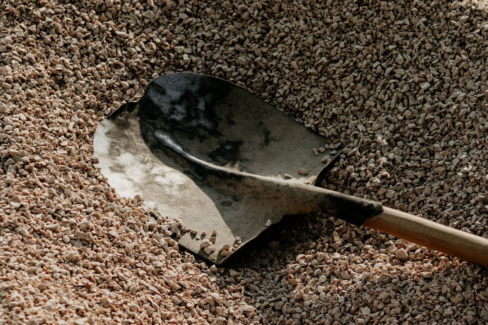 Steel shovel resting in a pile of crushed stone used as paver base gravel