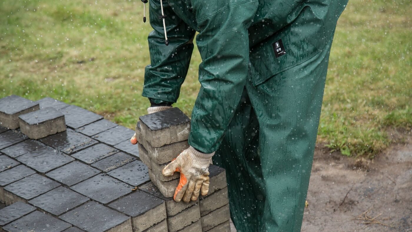 Installer in rain gear picking concrete pavers off a stack during a paver installation