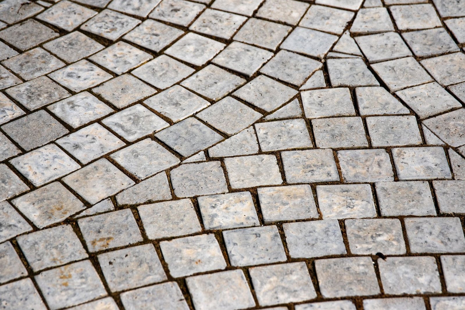 Close-up of granite setts laid in curved rows with open joints between the stones, typical of natural stone paving with wide joints