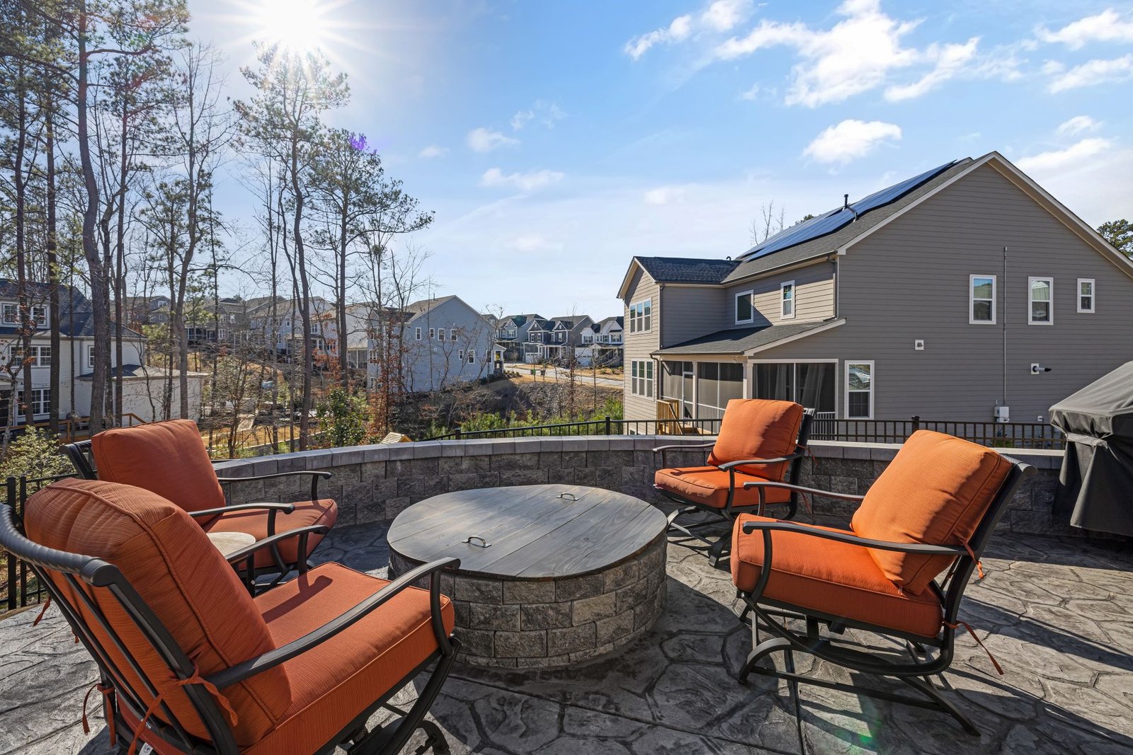 Raised paver patio with a stone seat wall and fire pit, built up above a sloping yard with views over the neighborhood