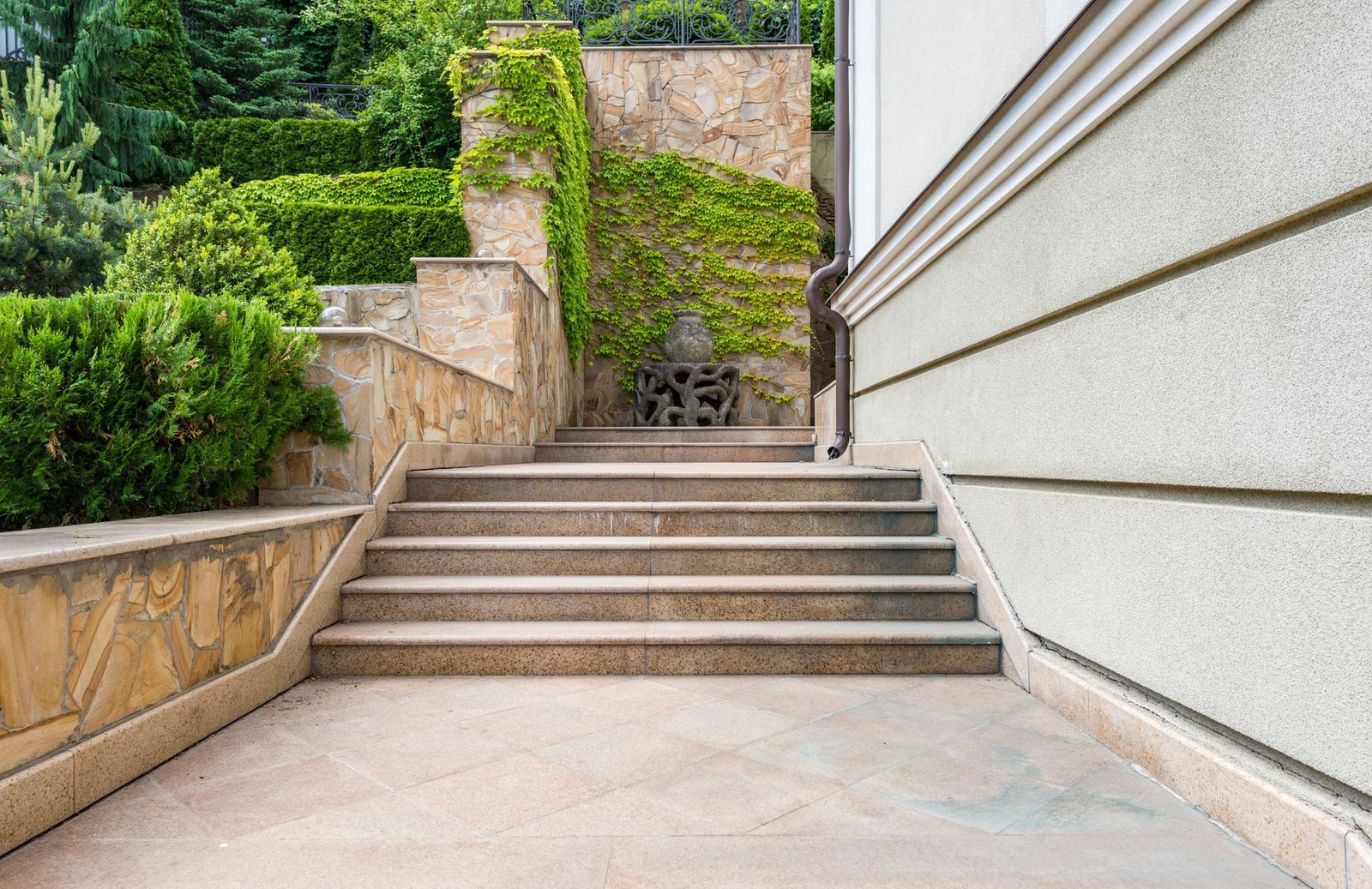 Stone steps climbing between planted retaining walls beside a house, a sloped walkway broken into steps