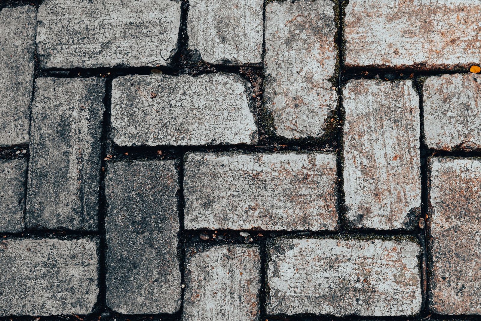 Worn herringbone pavers with open, dirt-filled joints that need cleaning out and re-sanding