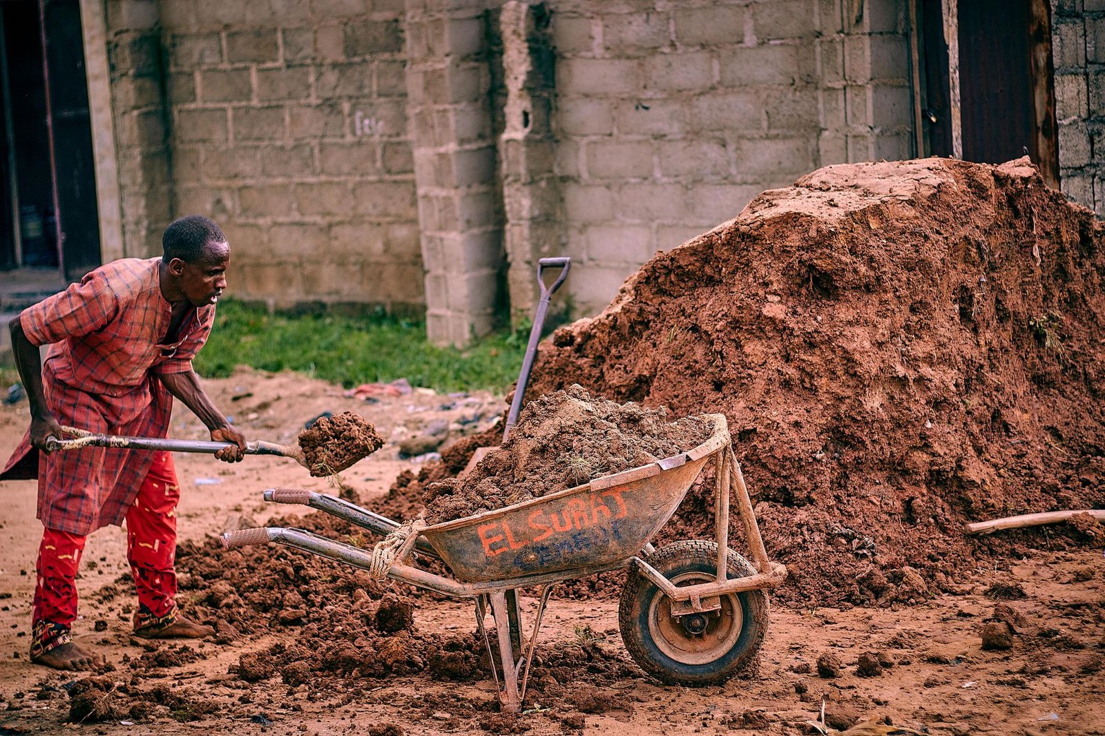 Worker shoveling soil from a pile into a wheelbarrow, the basic excavation tools for a paver patio