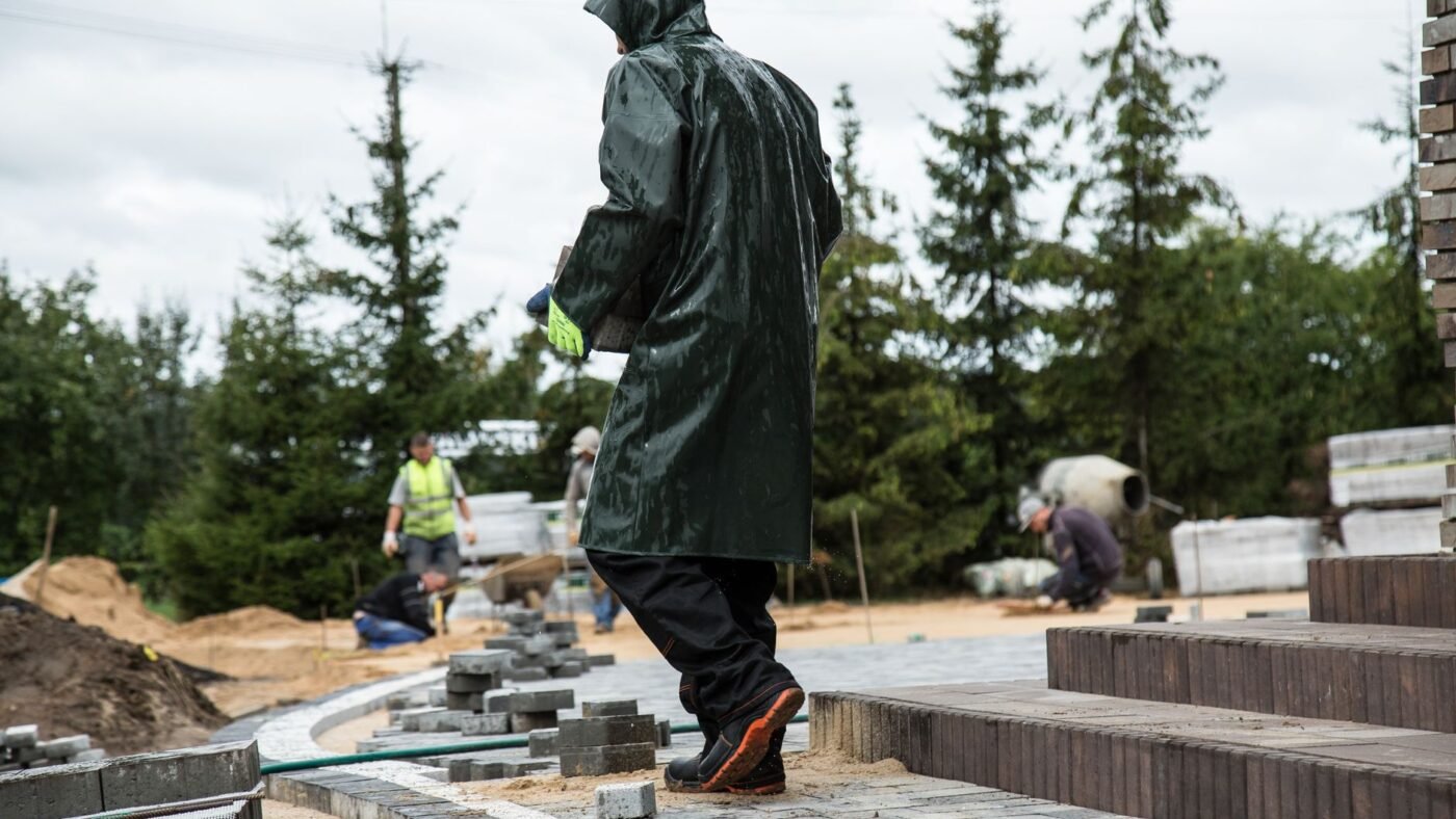 Paver patio job site with stacks of concrete pavers, a worker walking across the laid pavers and a crew setting steps behind