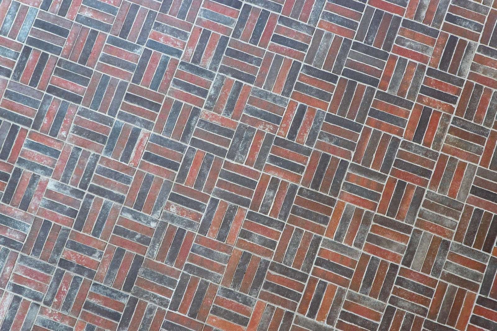 Red and gray brick pavers laid in a basketweave paver pattern, with groups of pavers alternating direction across the surface